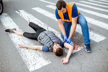 Man applying first aid to the injured bleeding person, wearing tourniquet on the arm after the road...