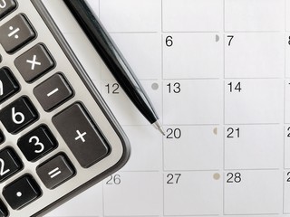 Business,finance, taxes, accounting, wages, payroll or money planning concepts : Top view or flat lay of calculator and pen on calendar