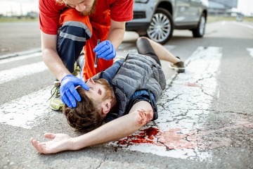 Medic checking unconscious person with flashlight, applying first aid to the bleeding person on the...