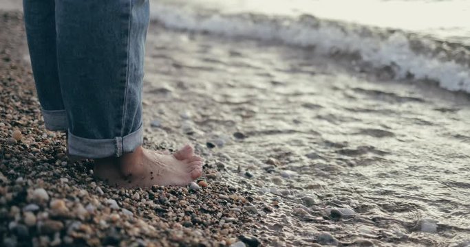 Closeup of girl's feet while standing at the beach in jeans 4k