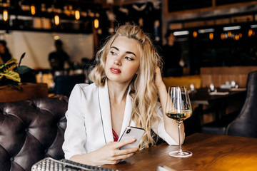 Beautiful young woman with a phone in her hand and a glass of wine relaxes in a restaurant