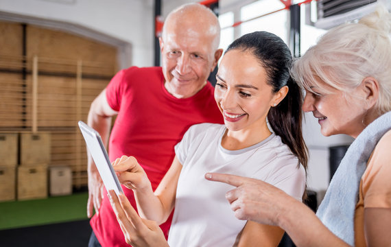 Personal trainer showing results of training on tablet to senior couple - Powered by Adobe