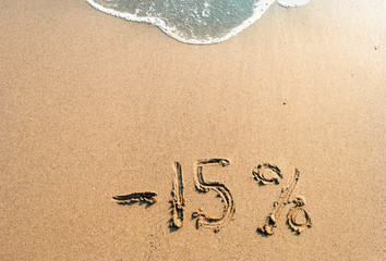inscription on the sand minus 15 percent, 15 %, sea wave on the sand with the inscription fifteen