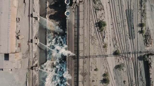 Aerial top down view; drone flying over railway line with a train of wagons-bucket with the slag; unloading of slag melt; cooling mass streams of water flowing from the holes on the edge of the quarry
