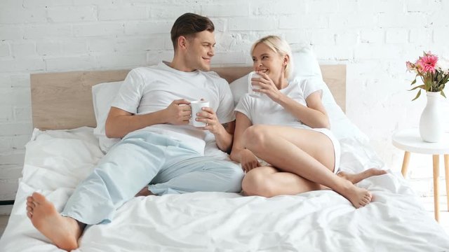 beautiful couple drinking coffee, talking and smiling in bed