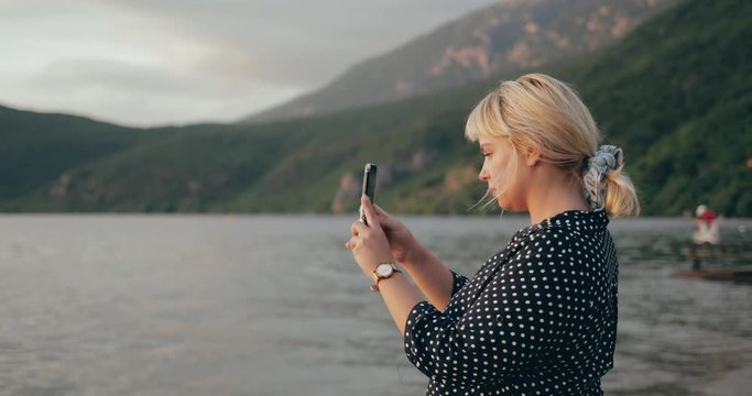 Blonde girl taking photos with smartphone at sunset on the beach 4K