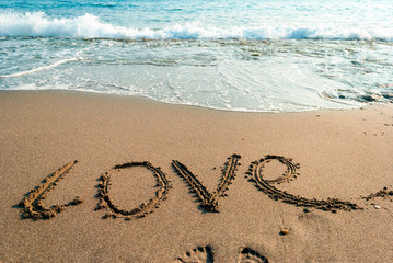 inscription love on the wet sand, a sea wave in the background