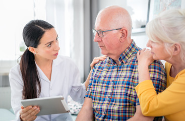 Nurse gives bad news to worried senior couple at home