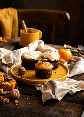 homemade tasty sweet orange pumpkin muffins or cupcakes with white cream, lavender, zest, nuts