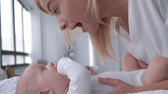 motherhood, blonde mom is talking and cute playing with her baby daughter who lies on the changing table close up