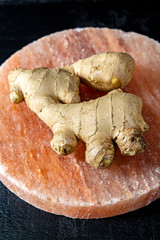 Fototapeta premium Fresh ginger roots on pink salt board close up on black wooden background