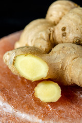 Fresh ginger roots on pink salt board close up on black wooden background