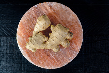 Fresh ginger roots on pink salt board close up on black wooden background