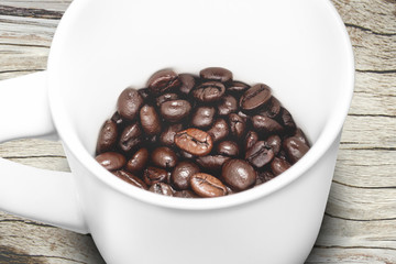 Roasted coffee beans in white cup and wood background