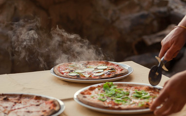 Chef cutting hot pizza in restaurant. Tasty pizza with with cheese and greens, closeup view. Popular italian food