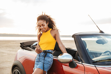 Happy smiling young pretty woman standing near car at the beach.