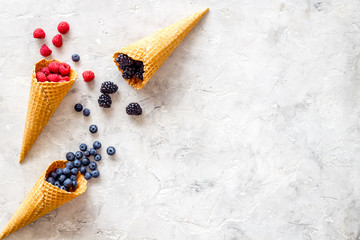 Fresh berries in waffle cones on light stone background top view mock up