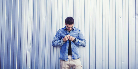 Stylish guy standing street in a denim jacket against metal wall 