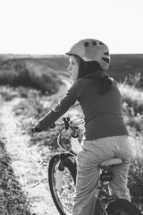 Little girl on a bike wearing a helmet on a dirt road in the field.