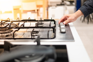 Male hand turning switch knob on modern gas stove in kitchen showroom. Cooking appliance in domestic kitchen. Home improvement and House interior design concepts