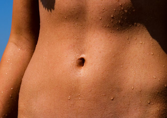 Fototapeta premium Beautiful athletic tanned belly with cute navel. A flat, slim, muscular and firm belly with a flawless bellybutton.