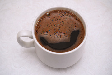 Hot black coffee with thick froth in a white cup on white table background