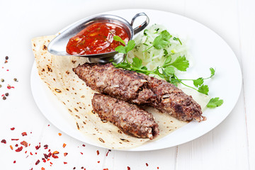 Close up view on grilled Lyulya kebab or Lule kebab. shashlik or barbecue meat on pita. Shish kebab, traditional georgian cuisine food. Copy space for design. Meat food with red sauce