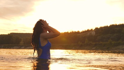 playful girl splashes her long hair in a refreshing summer evening near tropical island with refreshing river water. girl flips back hair. beautiful spray of water in rays of sunset. splash of water