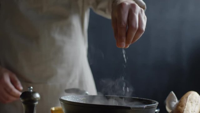 Close up of chef hand adding salt to hot pan on stove