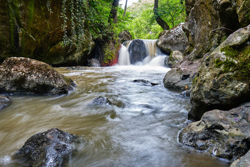 Naklejka na ściany i meble Long exposure photo of muddy water flowing between rocks in Tureni-Copaceni gorge, Romania.