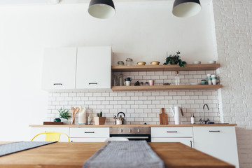 Modern new light interior of kitchen with white furniture and dining table.