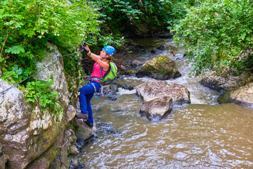 Female tourist wearing colorful sport clothing and via ferrata gear crosses a cable section in Tureni-Copaceni gorge, Cluj county, Romania.