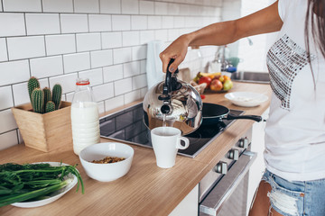 Woman pouring boiling water into a cup from kettle.