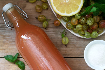 Gooseberry, lemon and mint syrup in a glass bottle and ingredients for syrup on a wooden table.