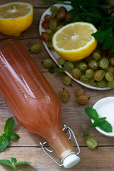 Gooseberry, lemon and mint syrup in a glass bottle and ingredients for syrup on a wooden table.