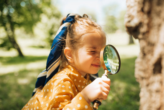 Cute curious kid with magnifying glass exploring the nature and insects outdoor. Adorable little girl playing in forest with magnifying glass. Child looking through magnifier on a sunny day in park