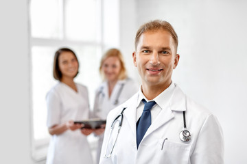 healthcare, medicine and profession concept - smiling male doctor in white coat at hospital