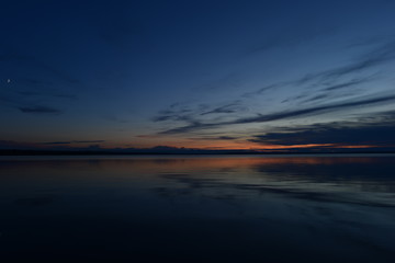 Blue sky in the light and shadows of twilight at the rising of the moon in the silence of the water of the lake