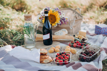 picnic tablecloth with a bottle of champagne and glasses, baguette, strawberries, cherries, cheese, wooden Board and a bouquet of wild flowers