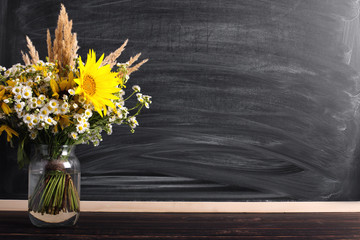 Teacher's day background. Black chalk board empty copy space and fresh wildflowers in vase. Holiday...