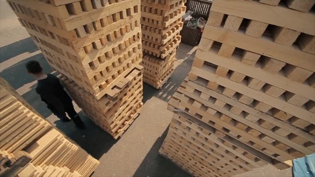 A young worker in uniform walks between wooden pallets in distribution outdoor warehouse. Slow motion. view from above