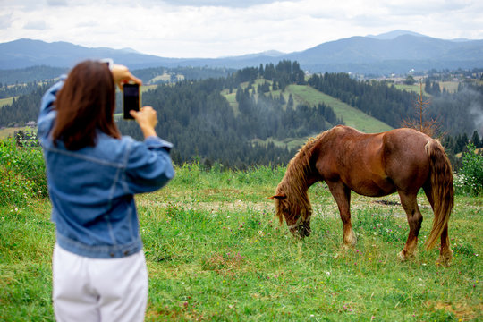 woman taking picture on phone of horse in mountains