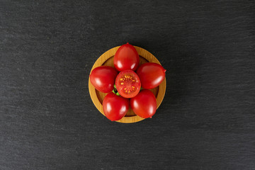 Group of five whole one half of fresh red tomato cherry on a bamboo plate flatlay on grey stone