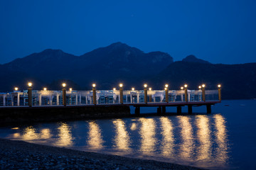 Romantic restaurant on the pier in the sea on mountains background in the evening