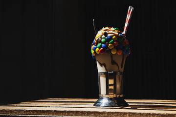 Homemade milkshake with whipped cream colorful candies and chocolate filling on a wooden table....