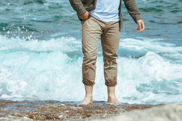 wet man legs in pants walking by sea rocky beach enjoying water