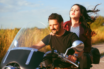 Couple on the background of the field rides a motorcycle. Traveling on bikes. Lifestyle, travel. Date. Sunset. Wind in the hair of a beautiful brunette. Extreme