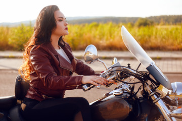 Beautiful brunette in a red leather jacket on a motorcycle in the field. Girl with beautiful hair