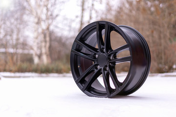 New stylish black brushed aluminum alloy wheel, on white snow. Winter.