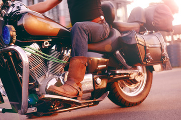 Biker riding on a motorcycle. Bottom view of the legs in leather boots. A man near the office...